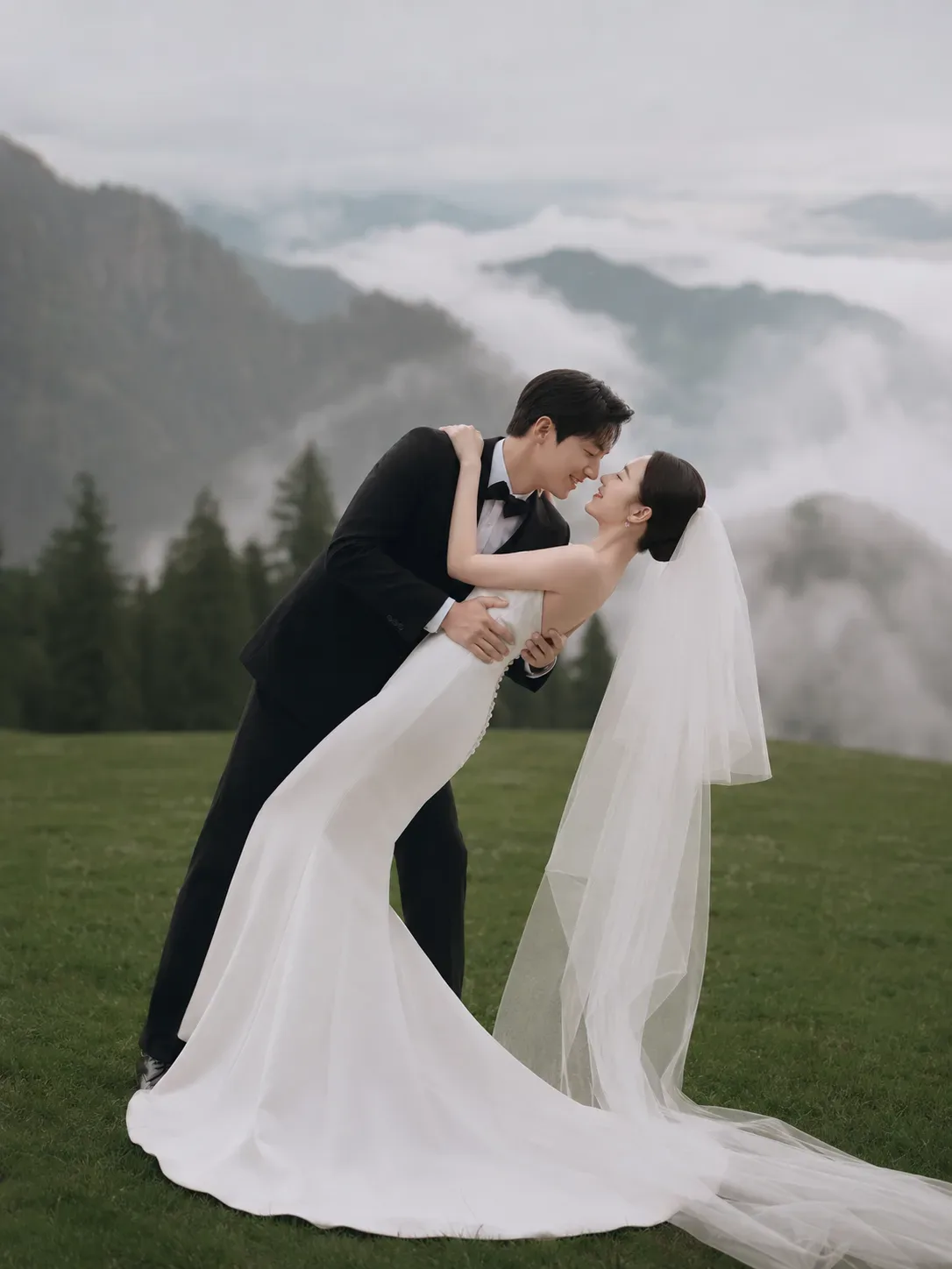 Josh dipping Hana for a kiss on a grassy hill, with mist rolling through the mountains behind them